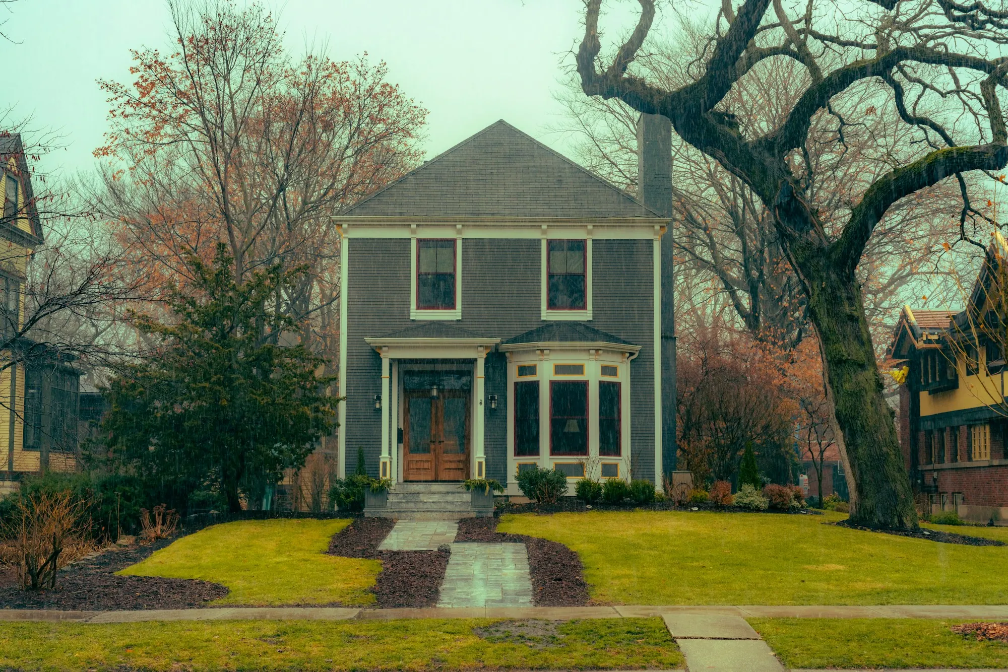 Gray two-story house with a center walk under big old trees